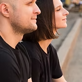 Un homme et une femme aux cheveux courts, tous deux vêtus de chemises noires, regardent vers le ciel,