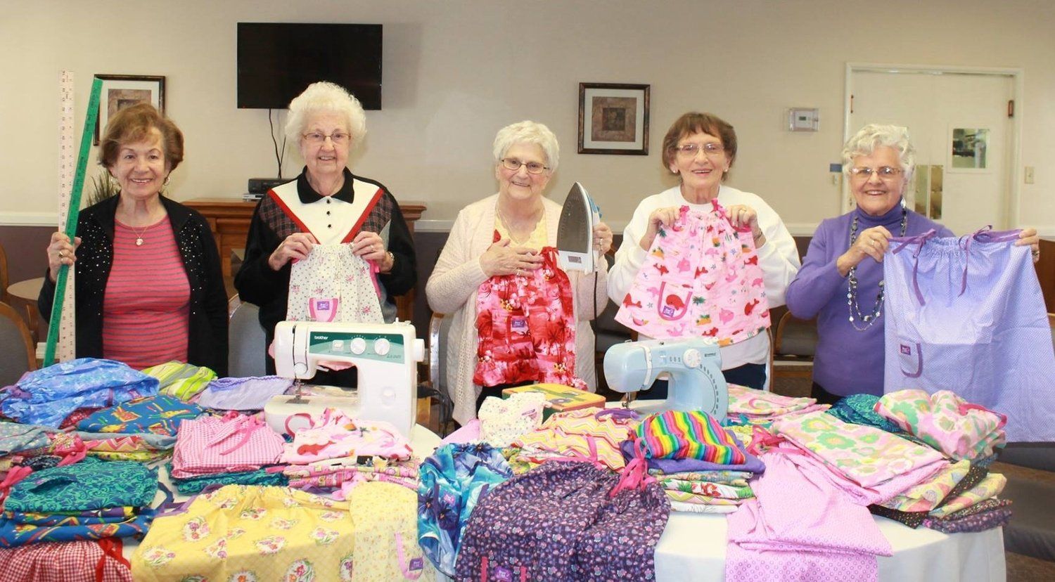 Five elderly women hold us items of clothing they have made.