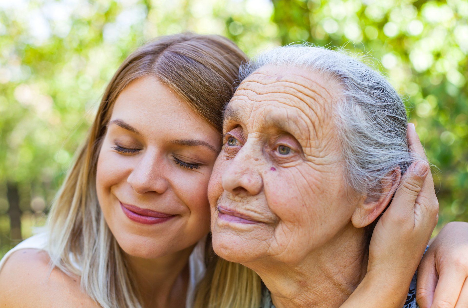 Woman hugs elderly woman outdoors; both smiling.