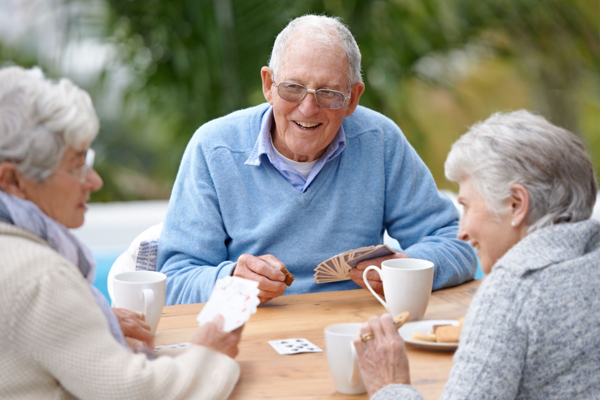 Older adults smiling while playing cards and sharing coffee outdoors, highlighting social connection