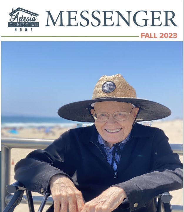 Elderly man in a wide-brimmed hat, smiling, in a wheelchair, at the beach. Artesia Christian Home Messenger cover.