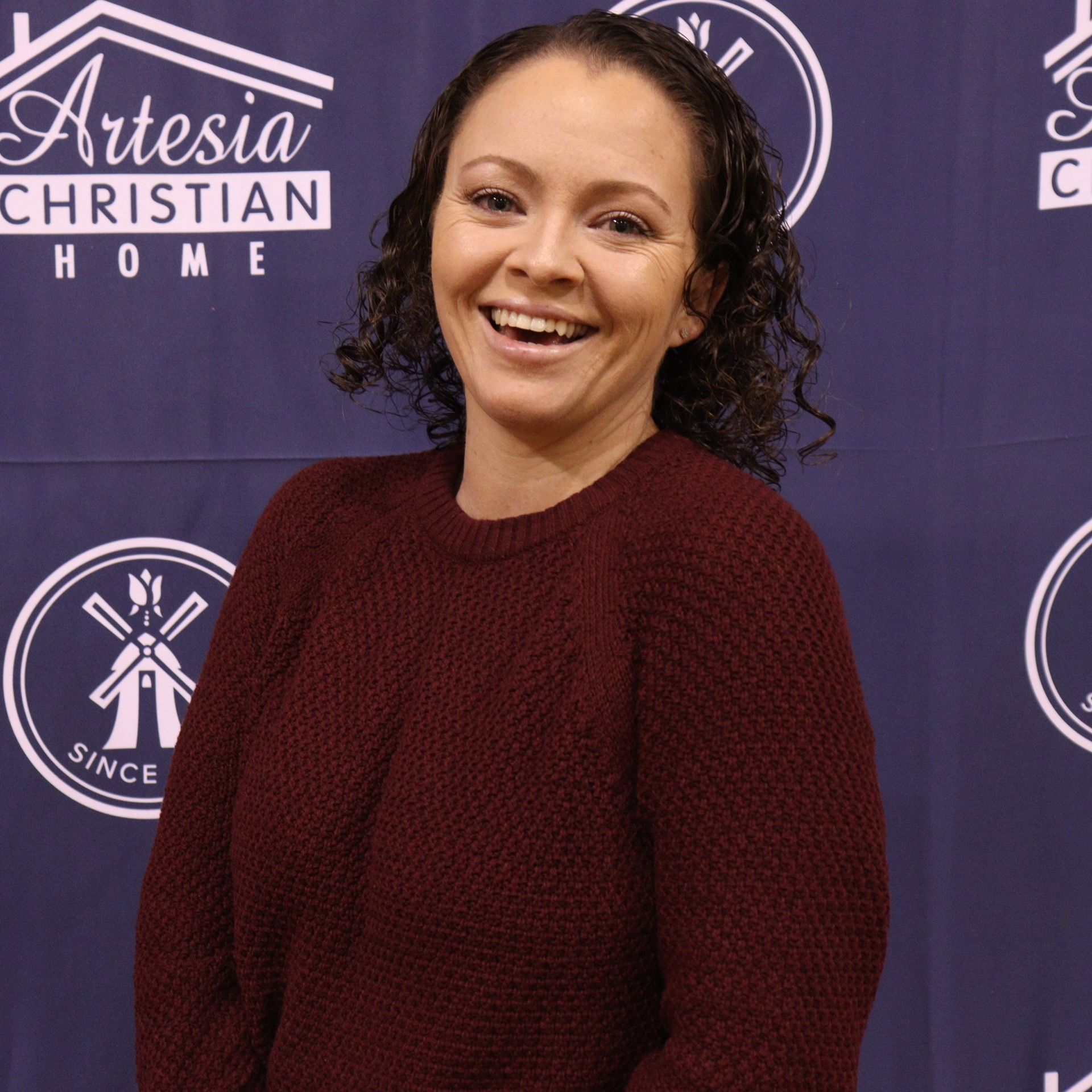 Woman with curly hair smiles, wearing a burgundy sweater.