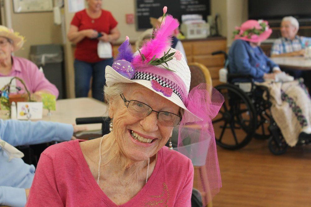 Elderly woman in a pink hat smiling, Easter celebration at a senior center.