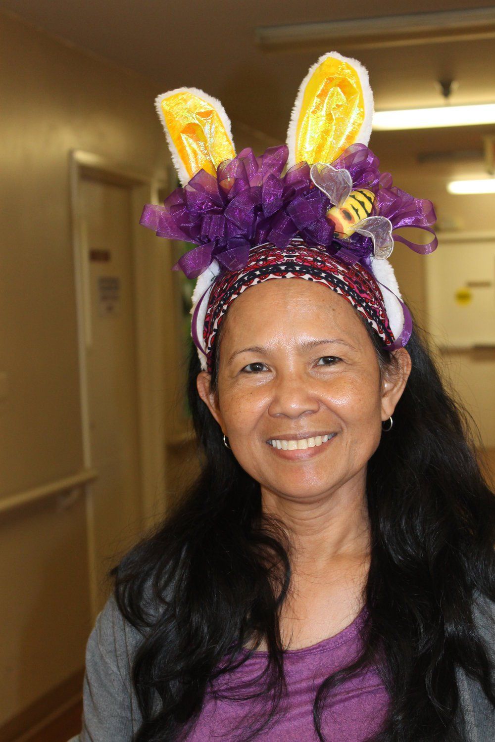 Woman with dark hair, wearing a purple and yellow bunny ear headband, smiling.