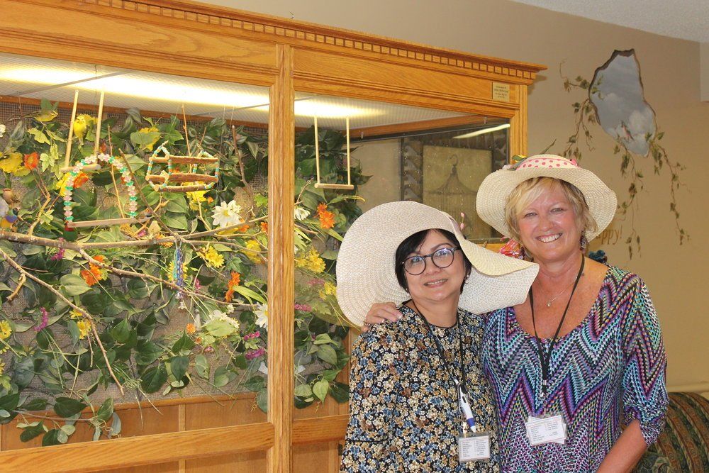 Two women smiling, wearing sun hats, posing near a decorative bird aviary.