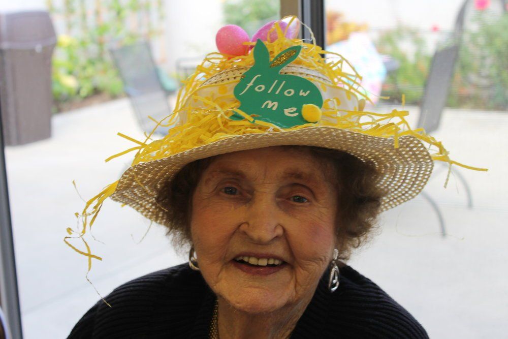 Elderly woman smiles, wearing straw hat with Easter decorations: eggs, bunny, 