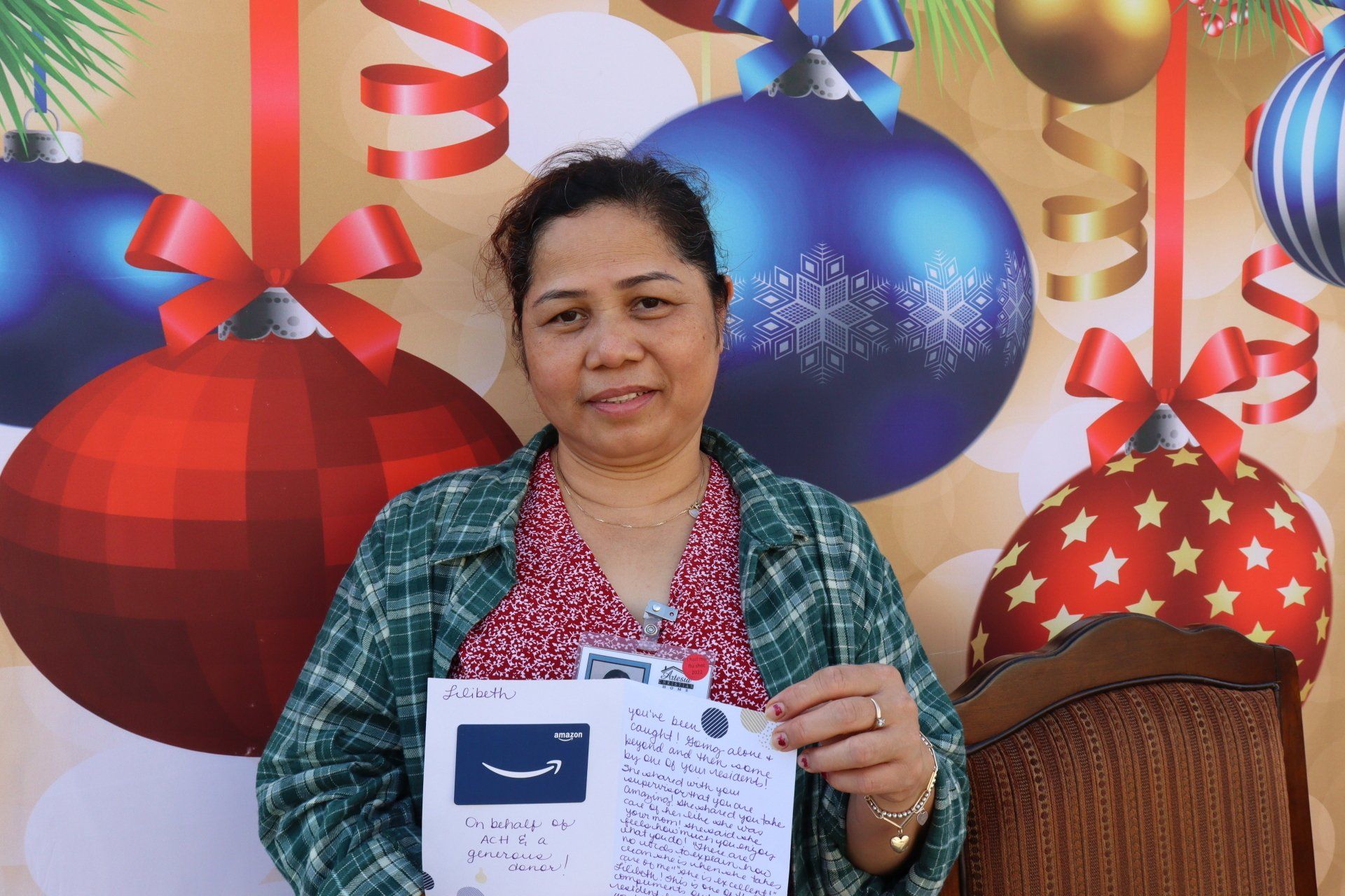 Woman holds a paper, smiles at the camera, with Christmas ornaments backdrop.