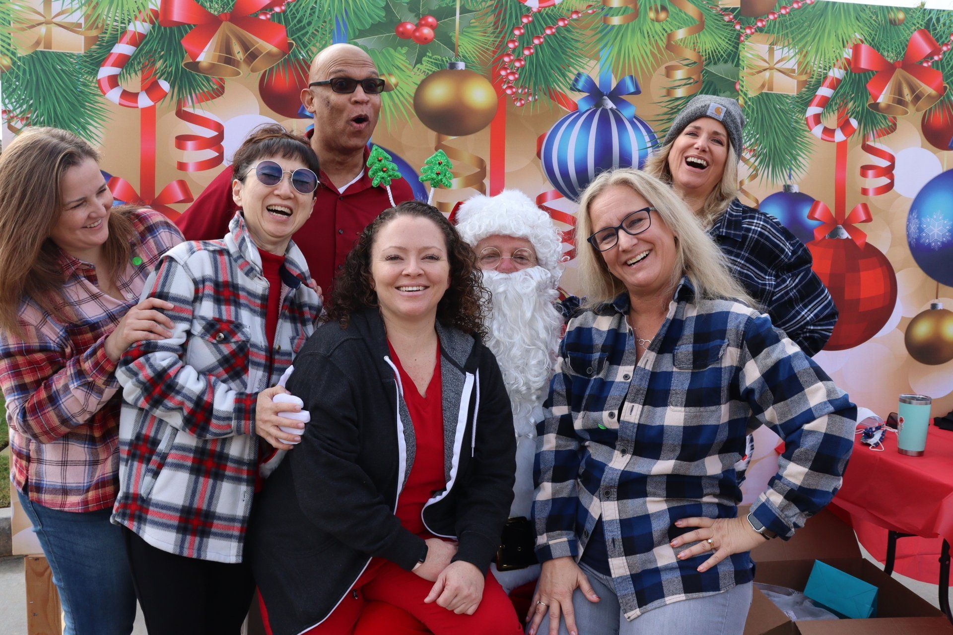 Group of people posing with Santa against a Christmas backdrop; smiles, holiday cheer.