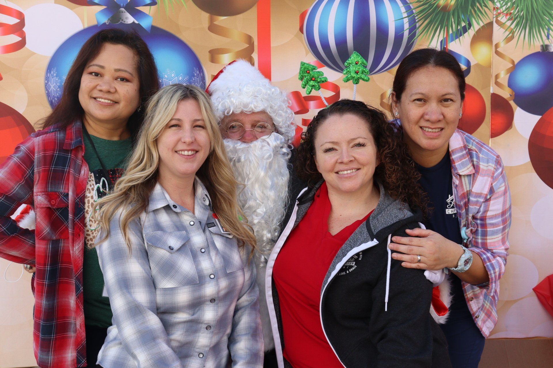 Five people pose with Santa against a festive backdrop; cheerful expressions.