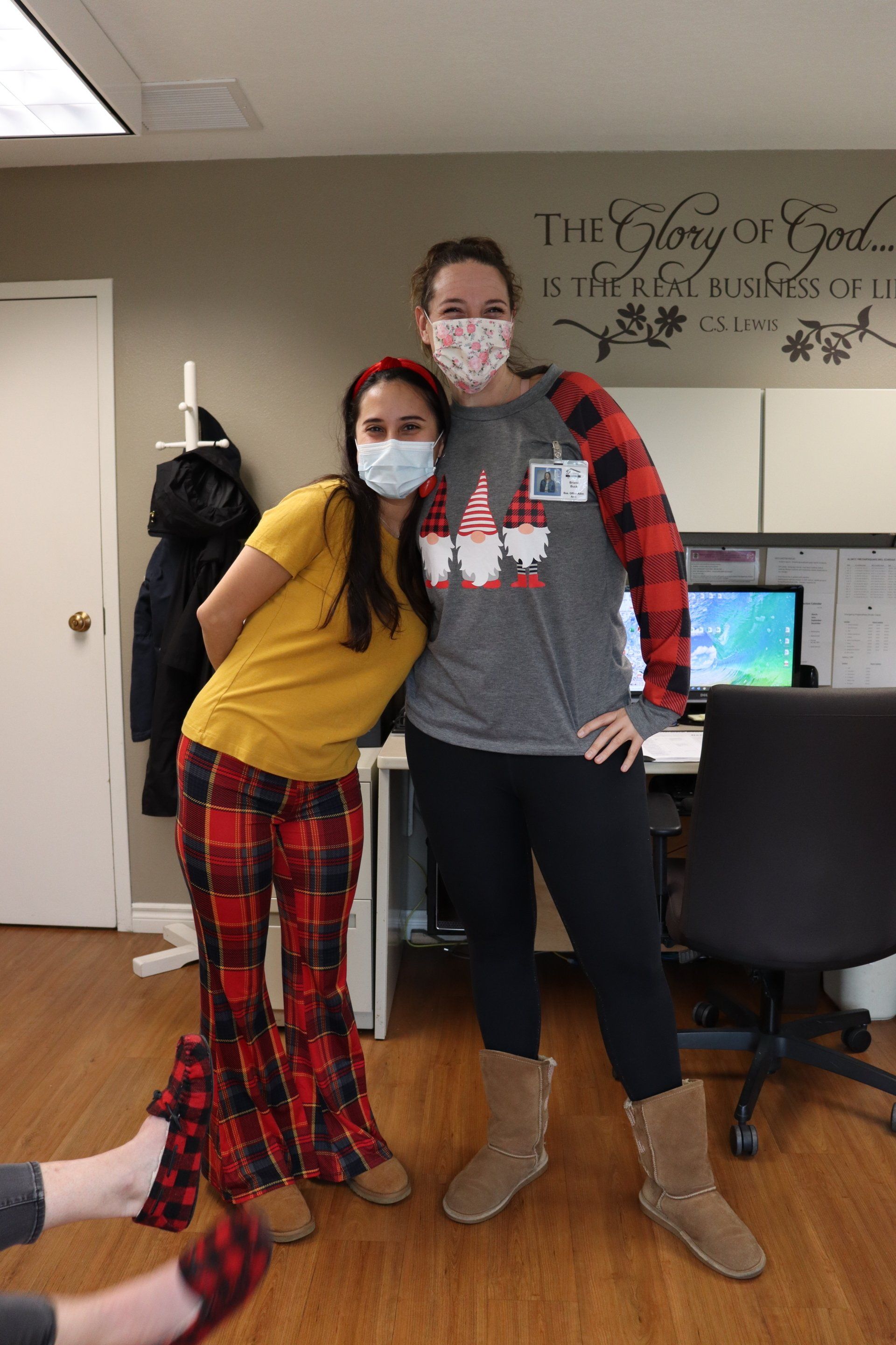 Two women in pajamas posing at an office; woman on left in red and black plaid pants; woman on right in gray shirt.