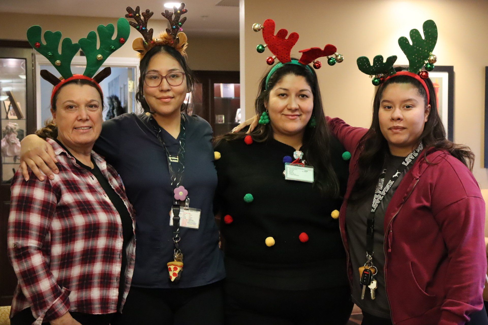 Four women wearing reindeer antlers, smiling, arms around each other, indoors.