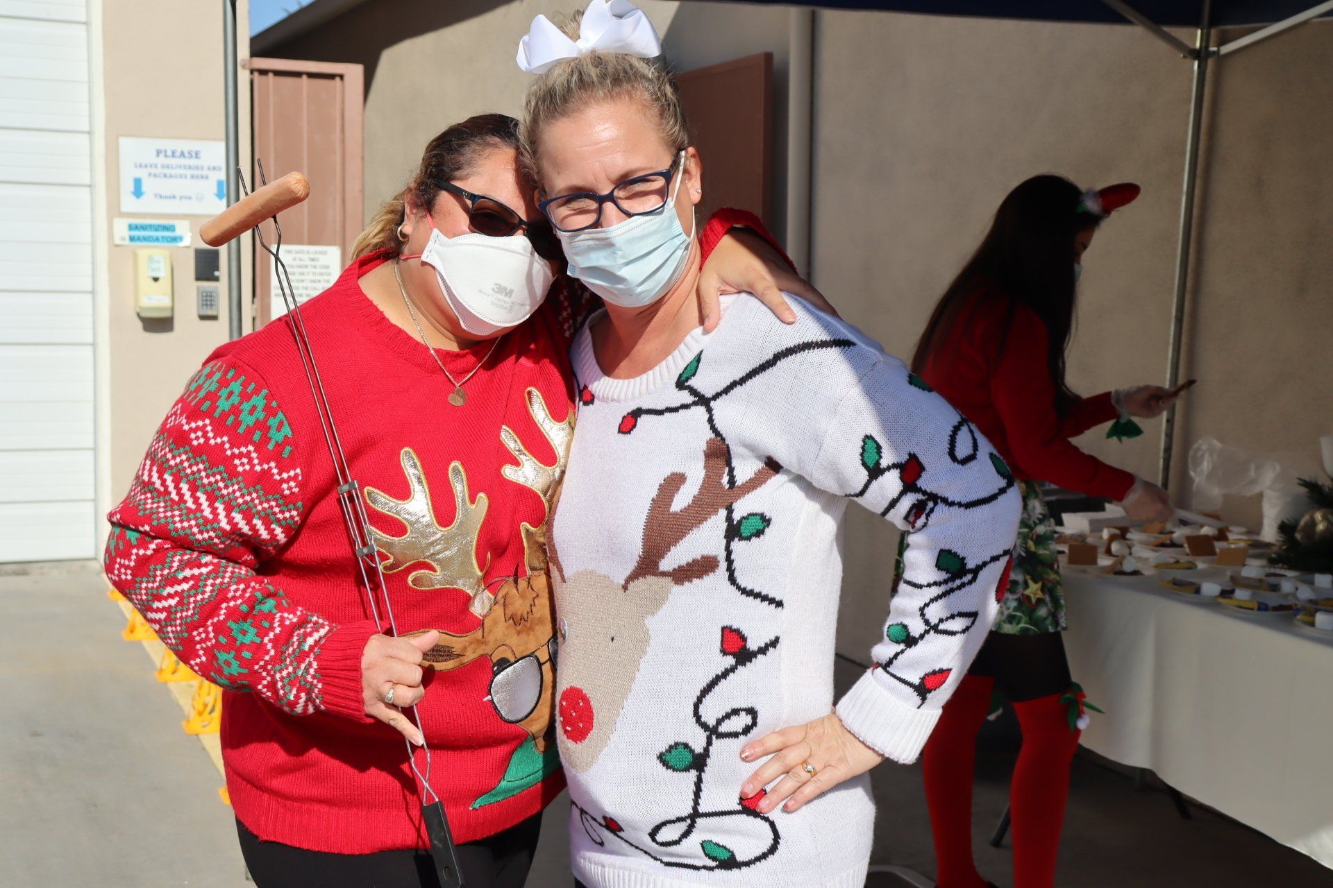 Two women in holiday sweaters pose outdoors, one with a white bow.