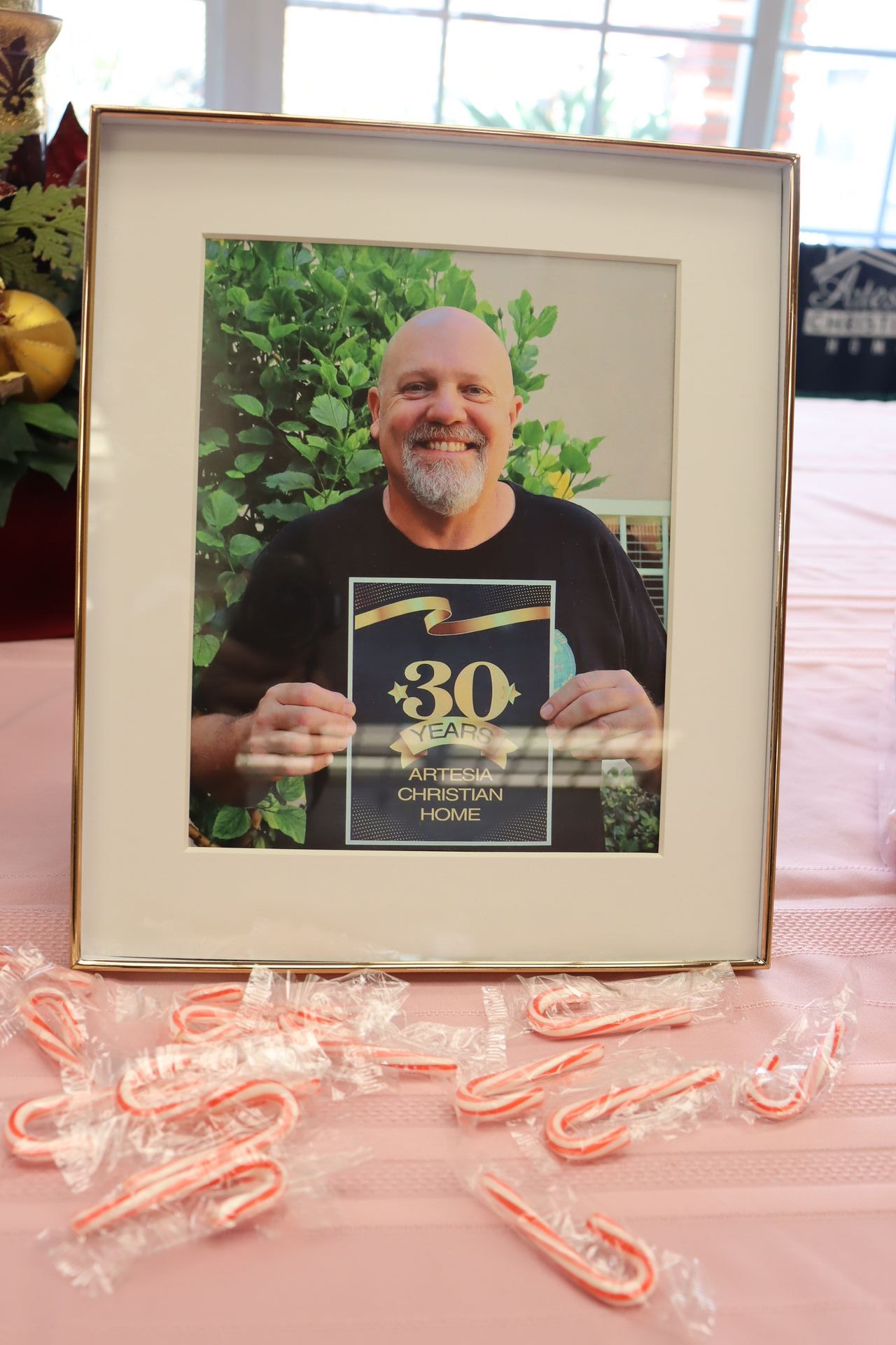 Man holding a 30-year service award photo in a frame on a pink tablecloth, surrounded by candy canes.