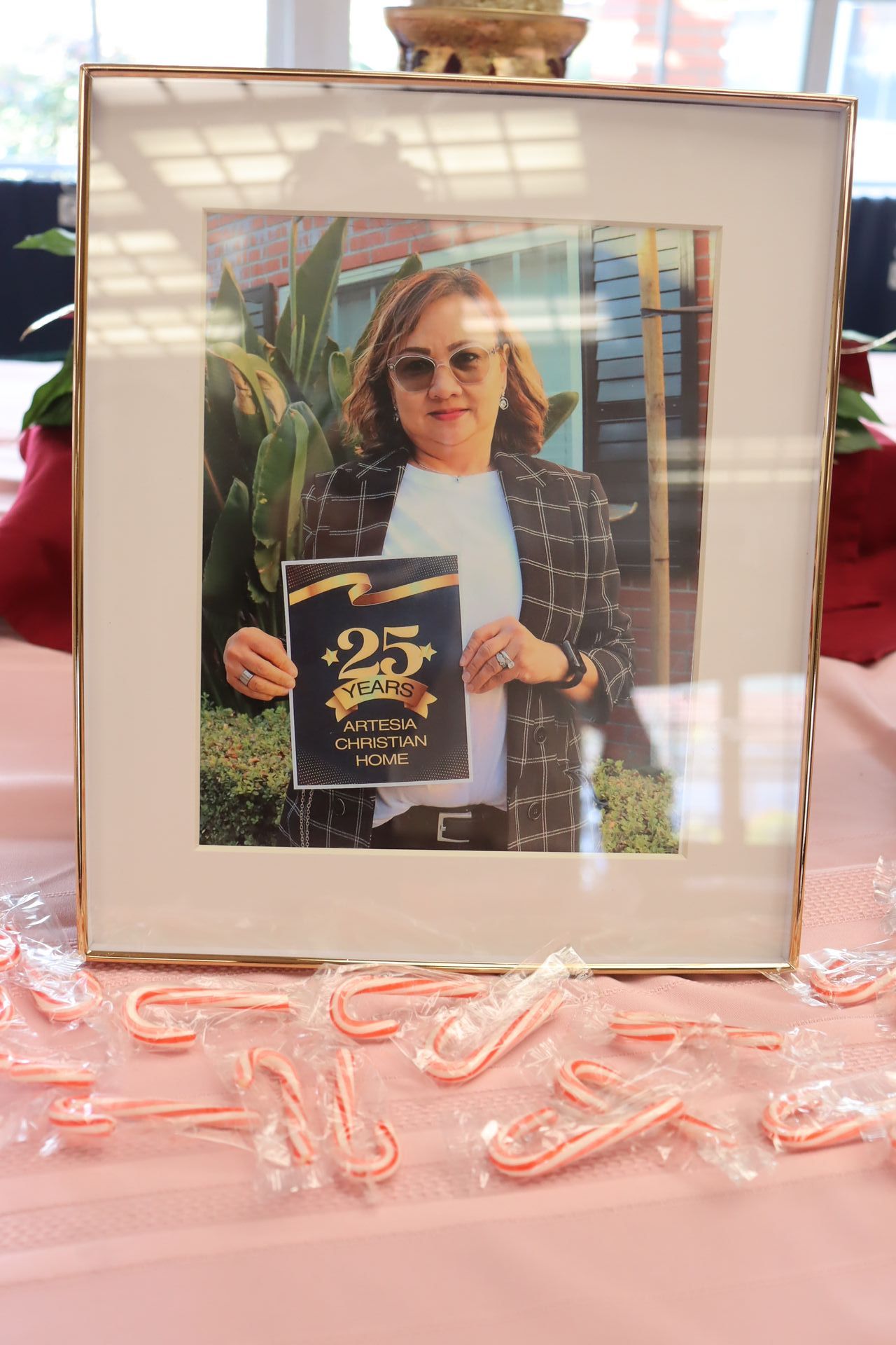 Woman holding award in framed photo on pink table with candy canes.
