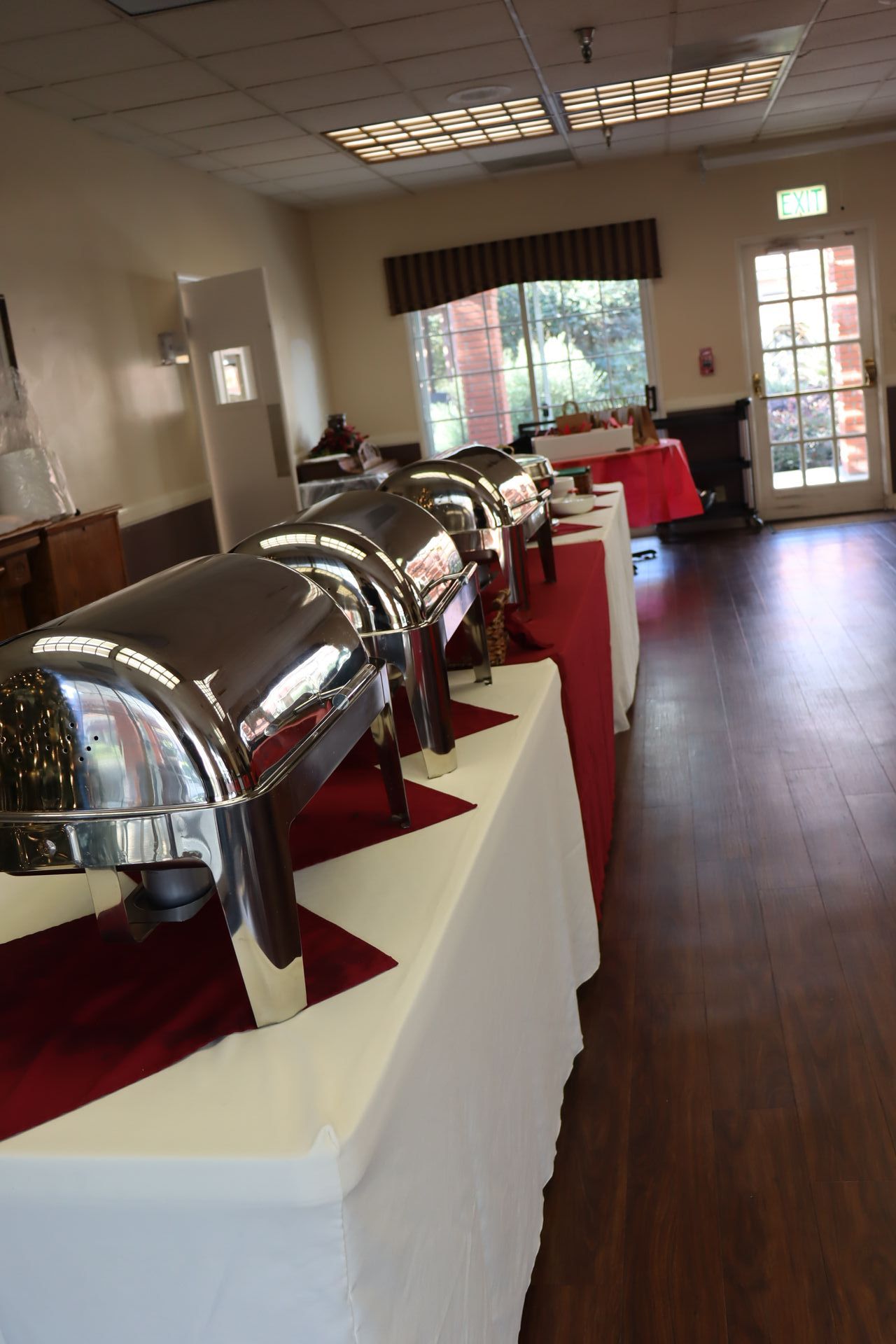 Buffet table with silver chafing dishes, white tablecloth, and red runner in a room.