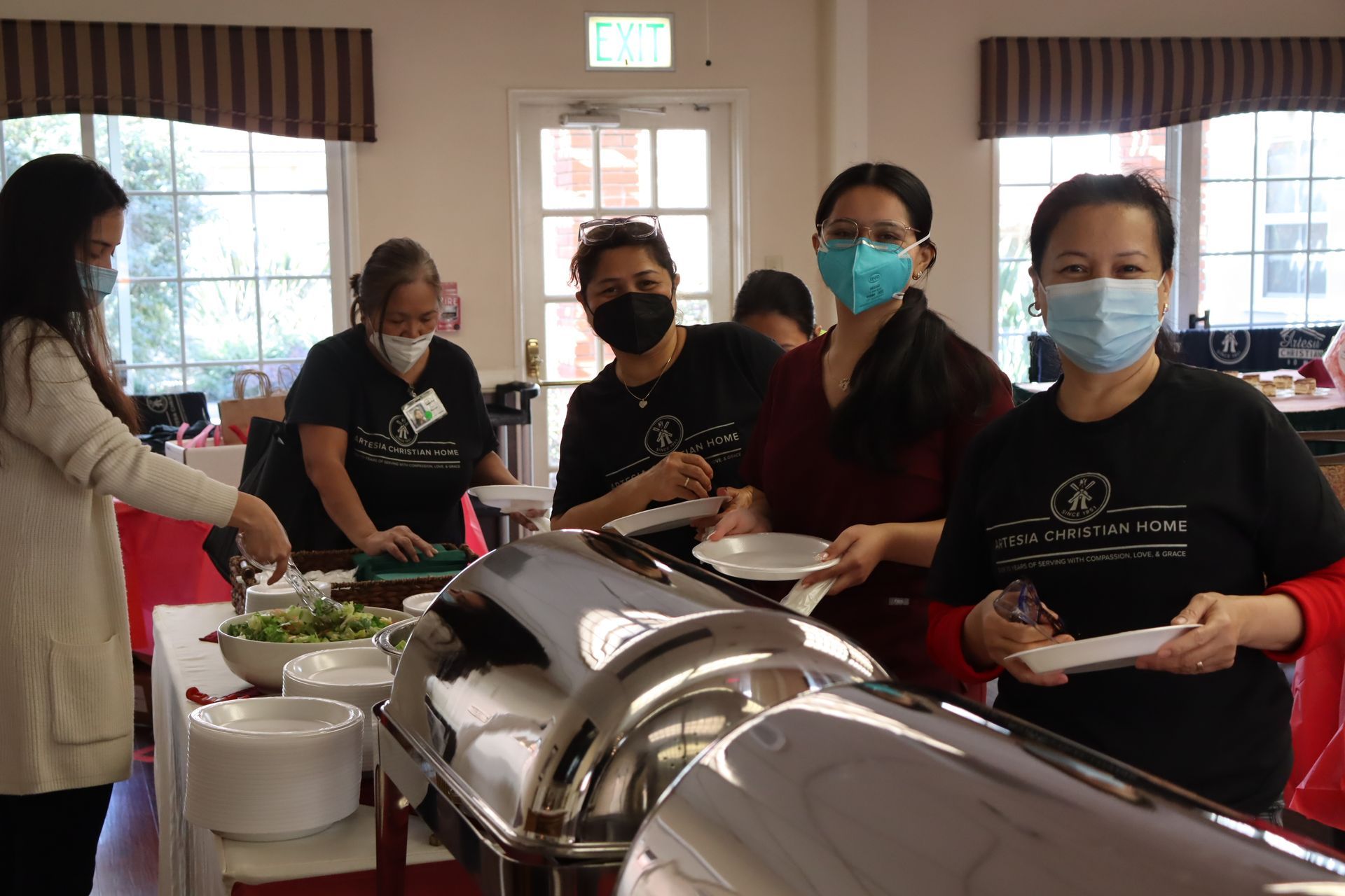 People at a buffet, some wearing masks, serving food at an event.