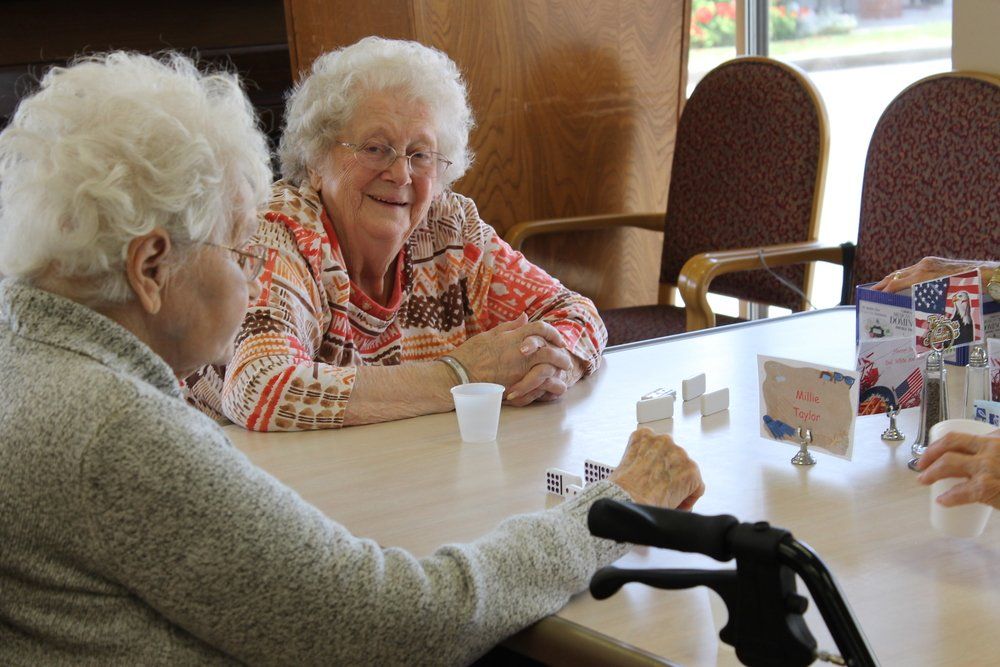 Two women with white hair play dominoes.