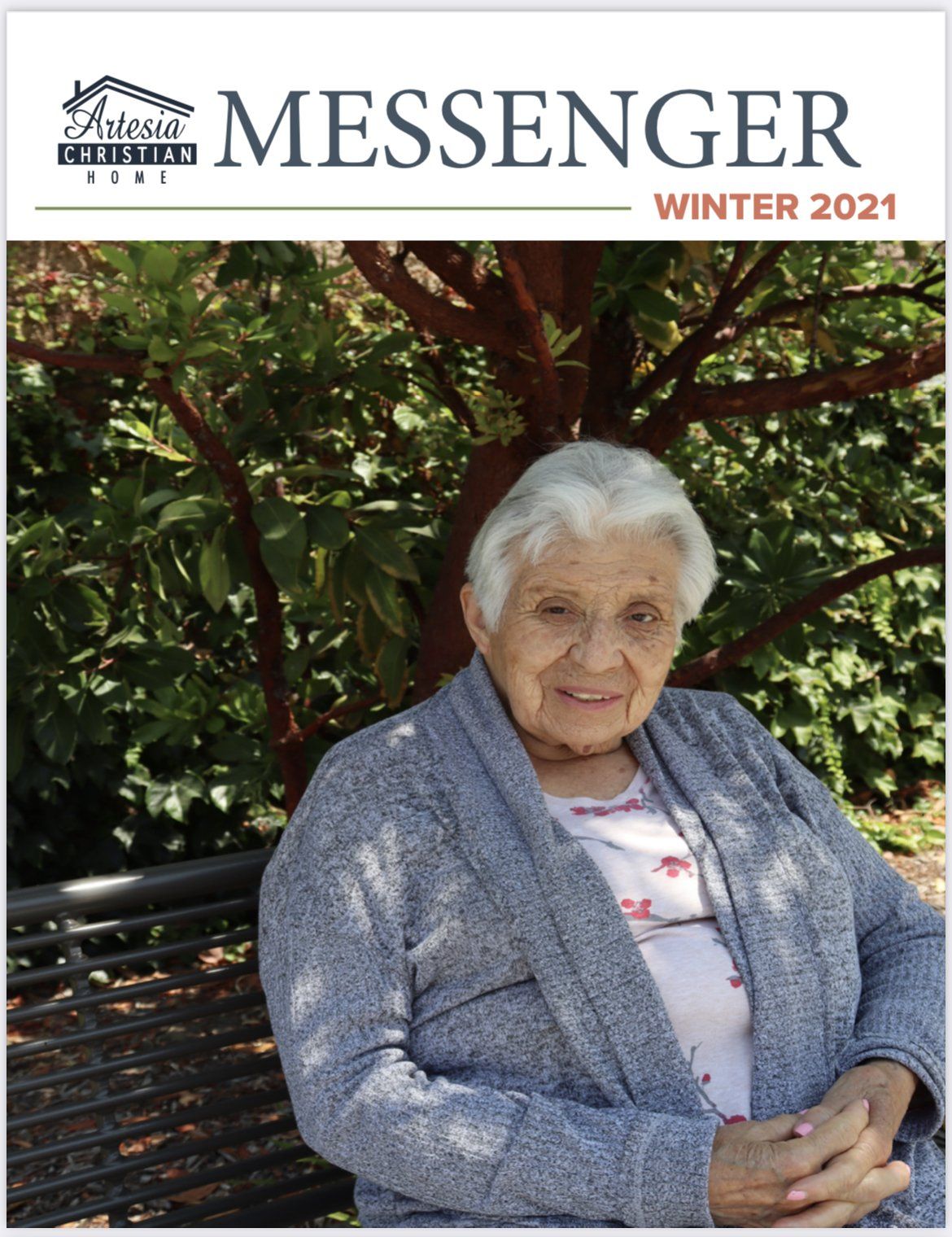 Woman in gray sweater smiles, sitting on bench in front of a tree.