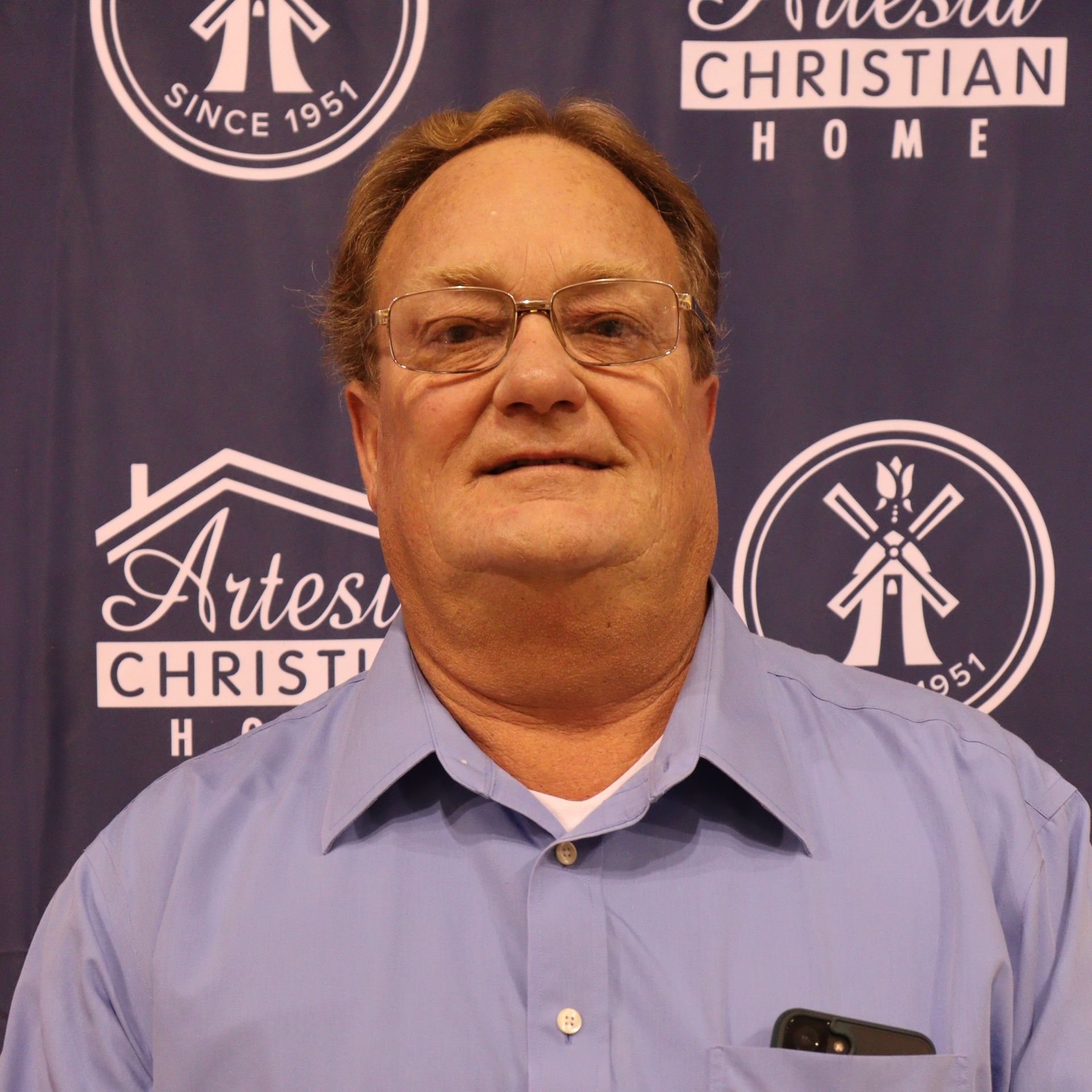 Man with glasses and blue shirt in front of Artesia Christian Home logo.