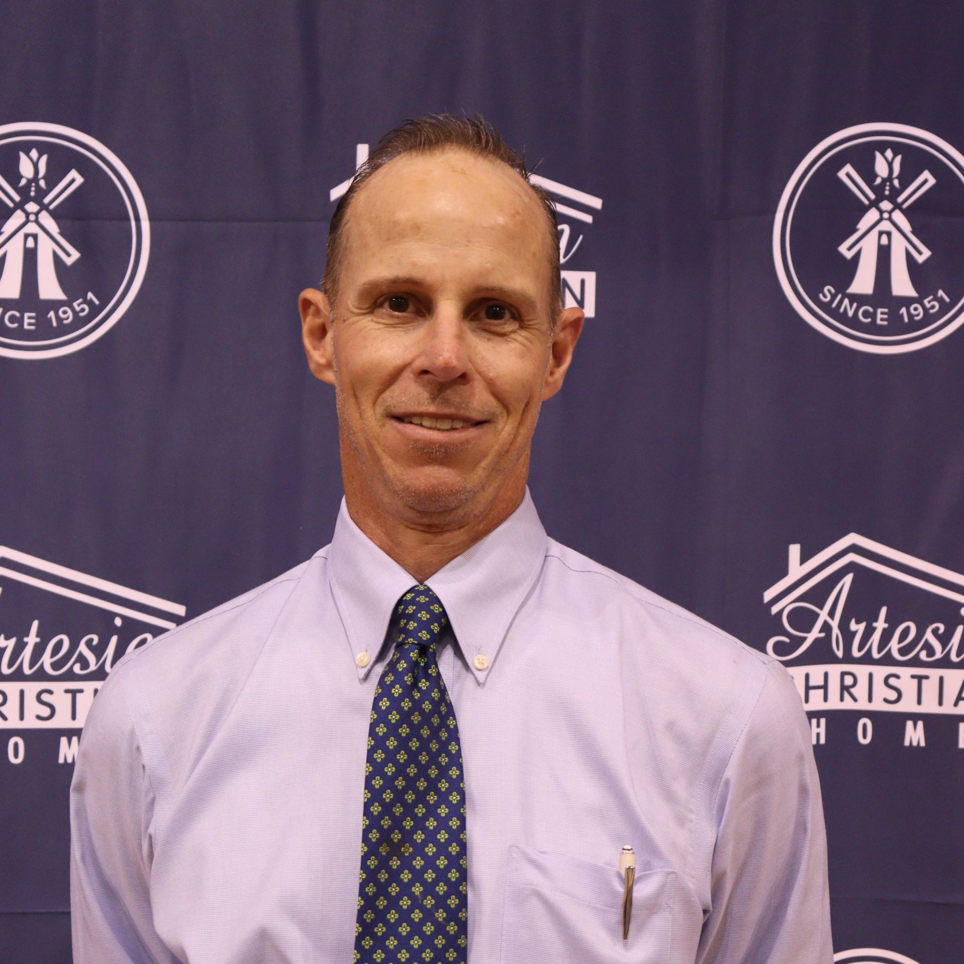 Man with tie, smiling in front of a backdrop for Artesia Christian Homes.