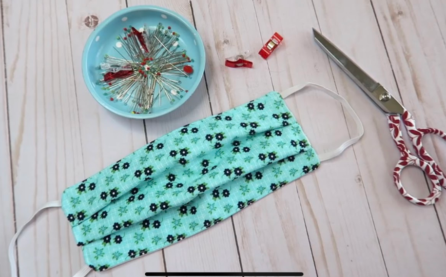 Blue floral face mask with pins, clips, and scissors on a wooden surface.
