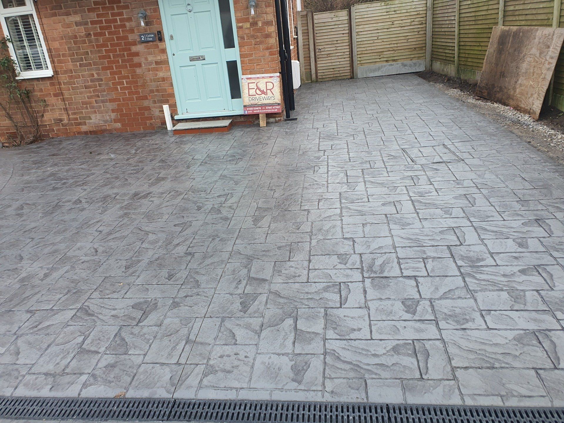 Gray patterned concrete driveway in front of a brick building with a teal door.