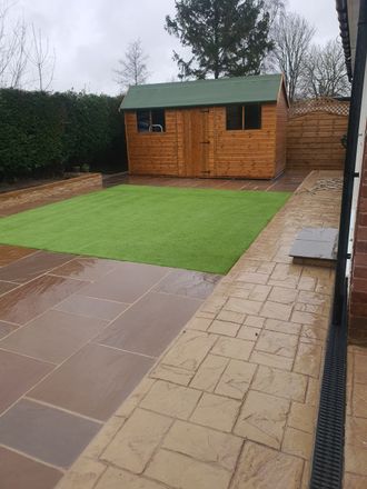 A backyard with a brown shed, green lawn, and brown stone patio. Overcast day.