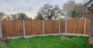 Wooden fence with concrete posts and a patch of green grass. Overcast sky and trees in the background.