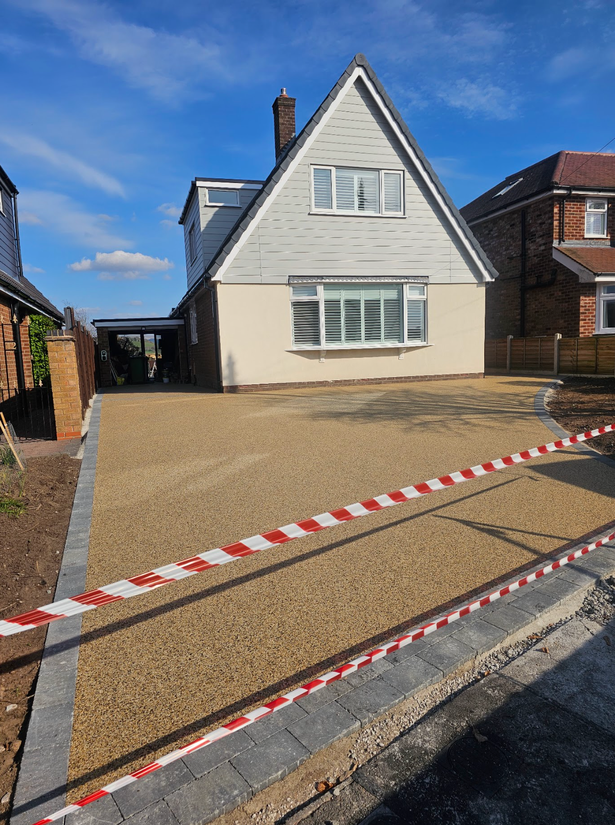 Gravel driveway in front of a house with a gray roof and light-colored walls. Caution tape marks the edge.