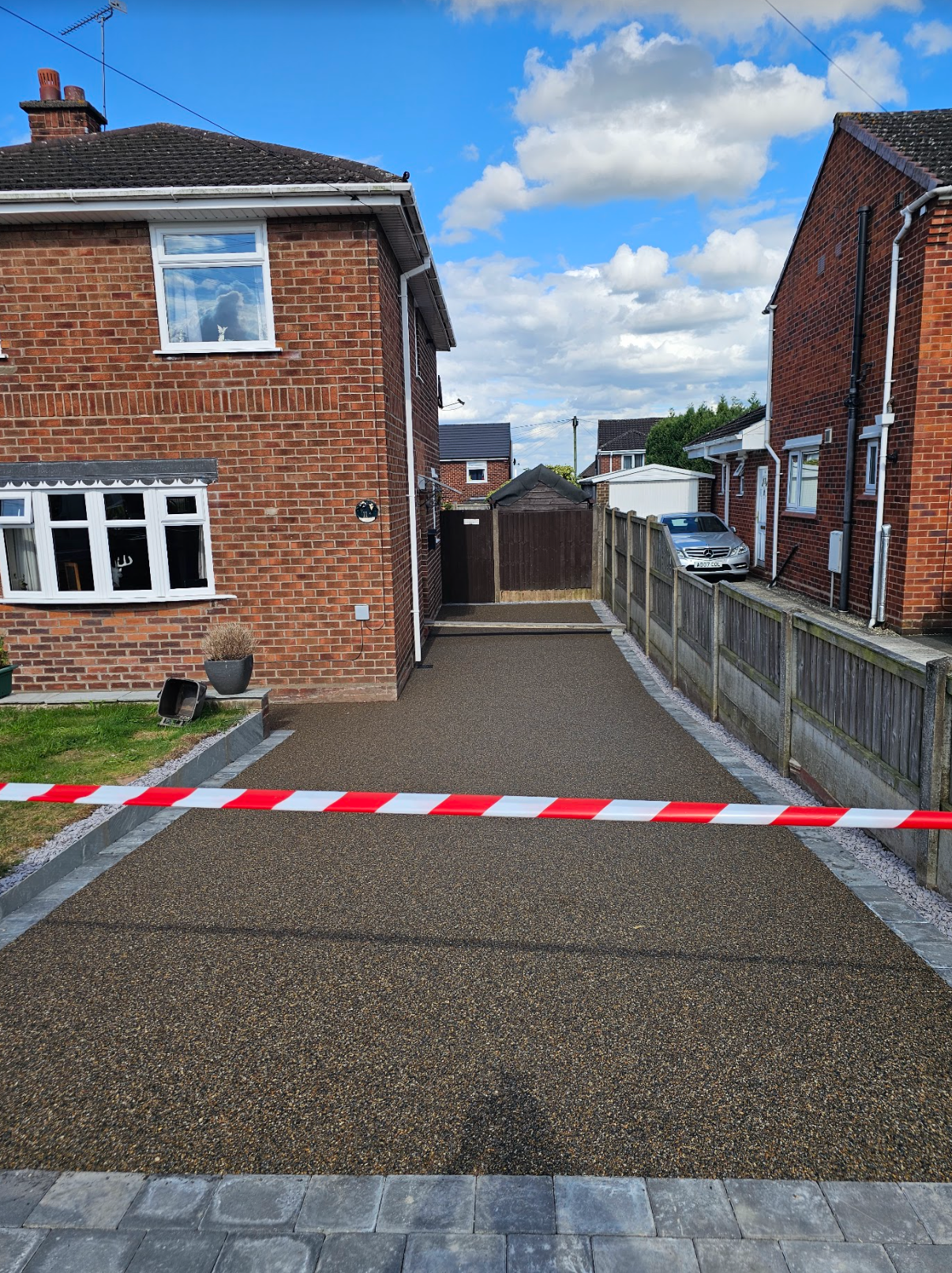 A newly paved driveway with red and white caution tape in front of a brick house.