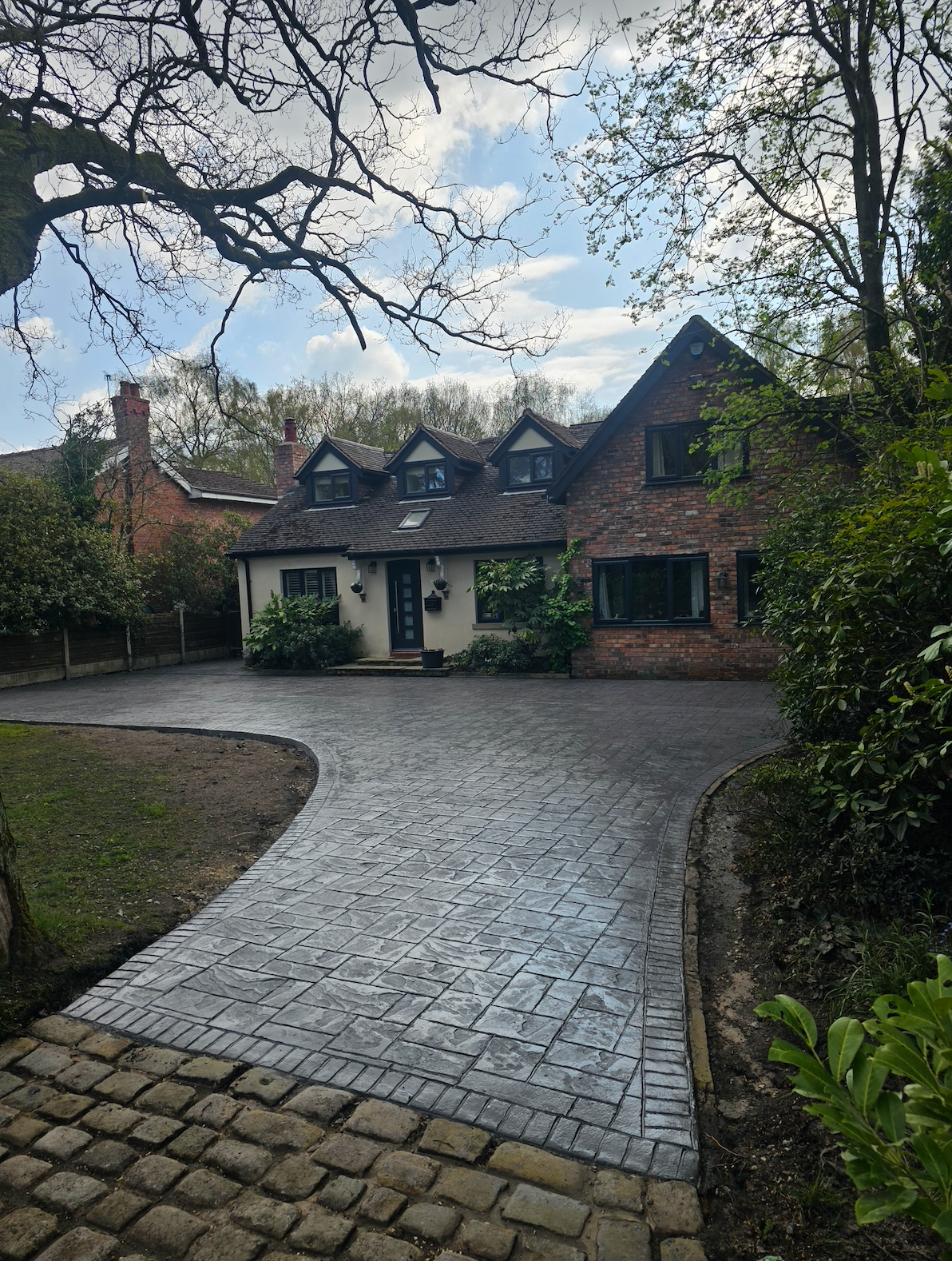 Brick house with gray cobblestone driveway under a cloudy sky.