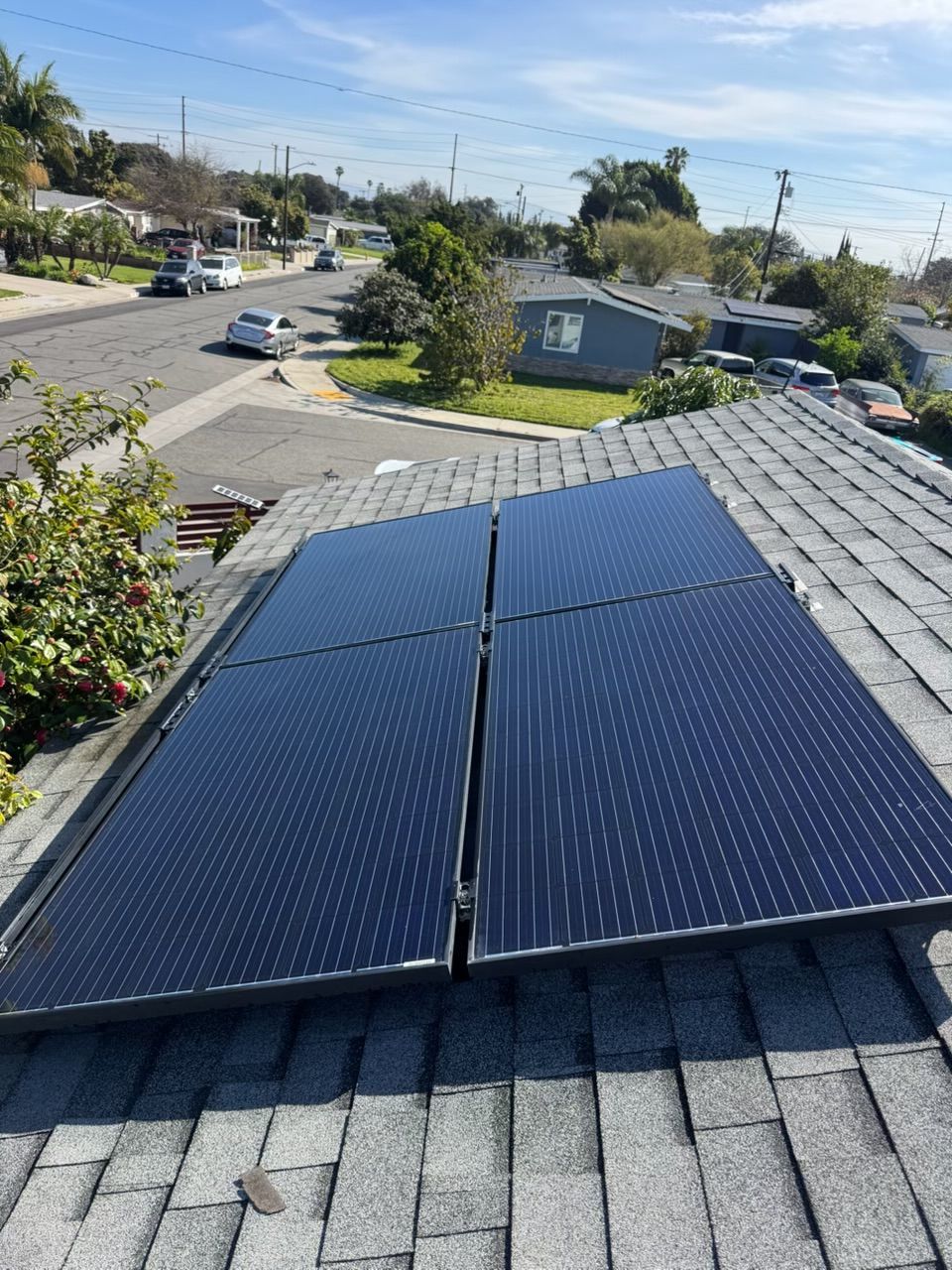 Solar panels mounted on a gray shingled rooftop in a suburban neighborhood