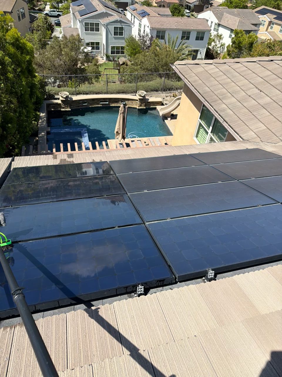 Solar panels on a rooftop overlooking a backyard pool and neighboring houses