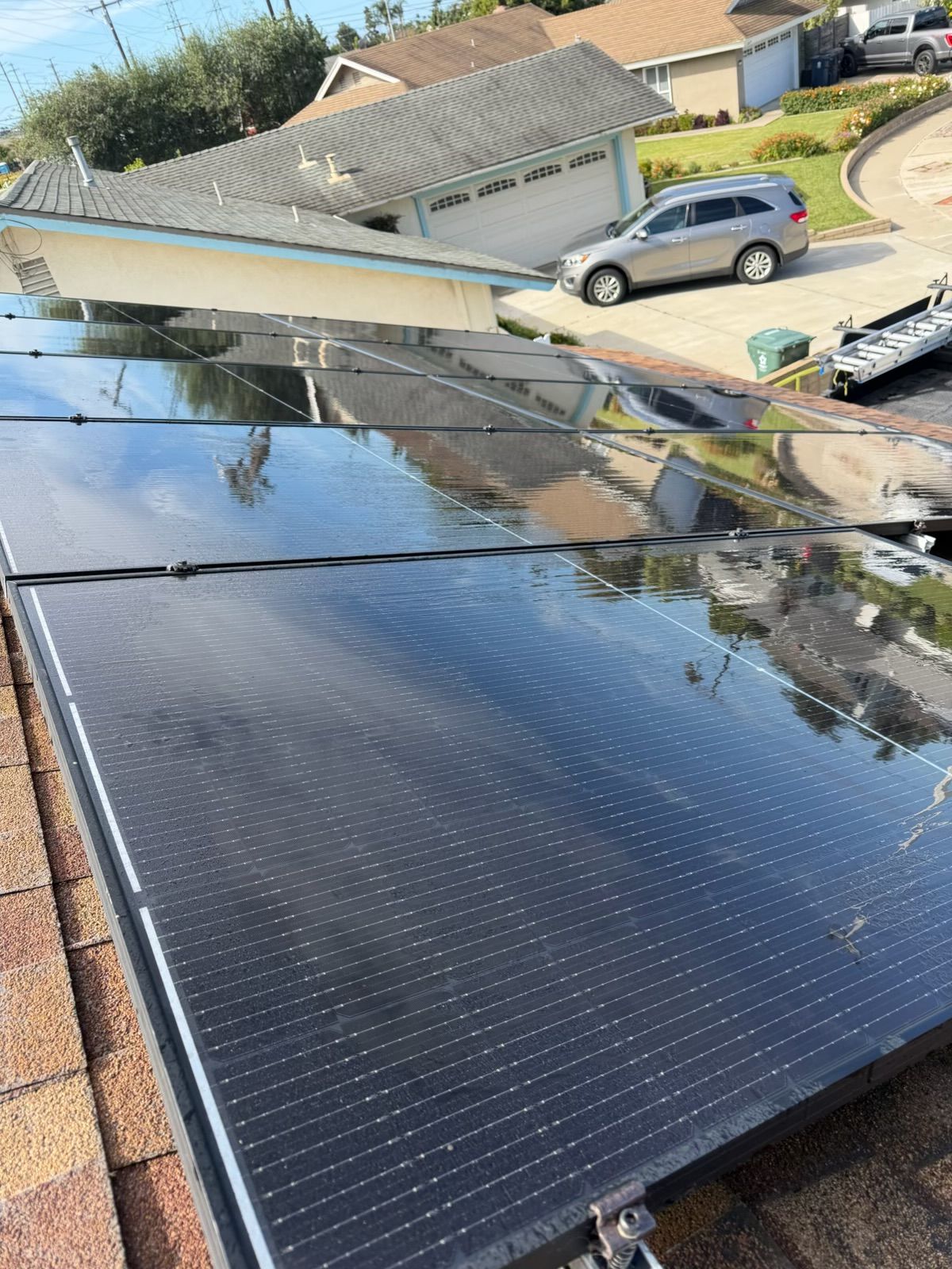 Solar panels installed on a sloped roof in a suburban neighborhood, with neighboring houses and a parked car nearby