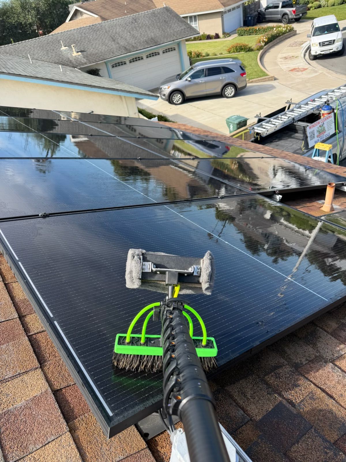 Solar panels being cleaned on a rooftop with a long-handled brush.