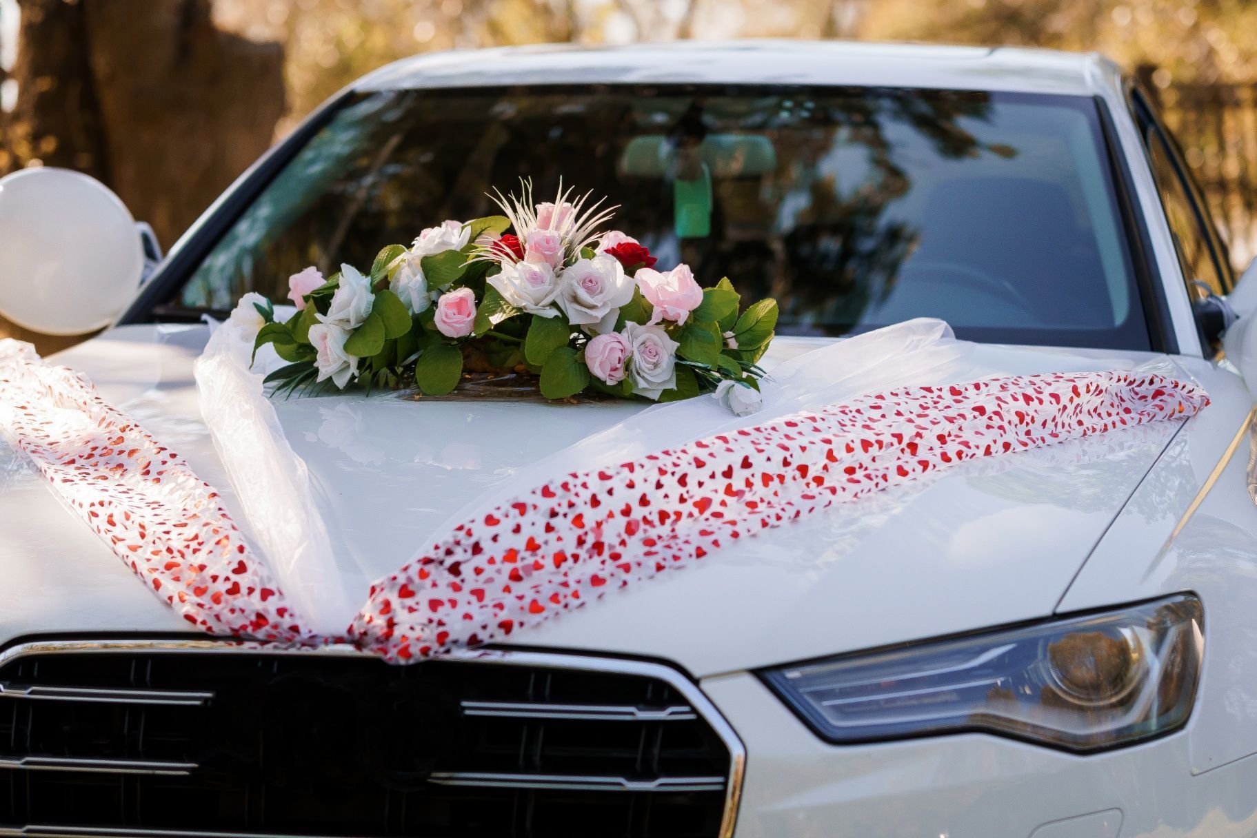 White car decorated for a wedding with flowers and ribbons on the hood.