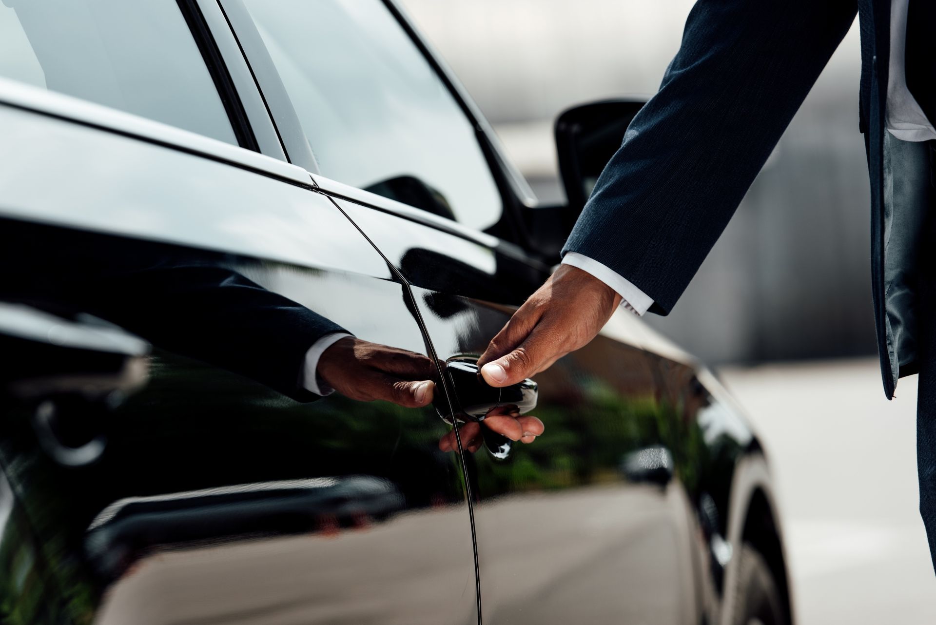 Person in a suit opening a black car door, holding the handle.