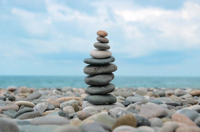 Stack of balanced stones on a beach, blue sea and sky in the background.