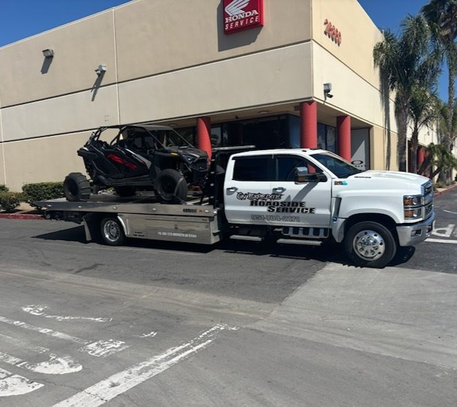 White tow truck with a black off-road vehicle, parked in front of a Honda dealership.