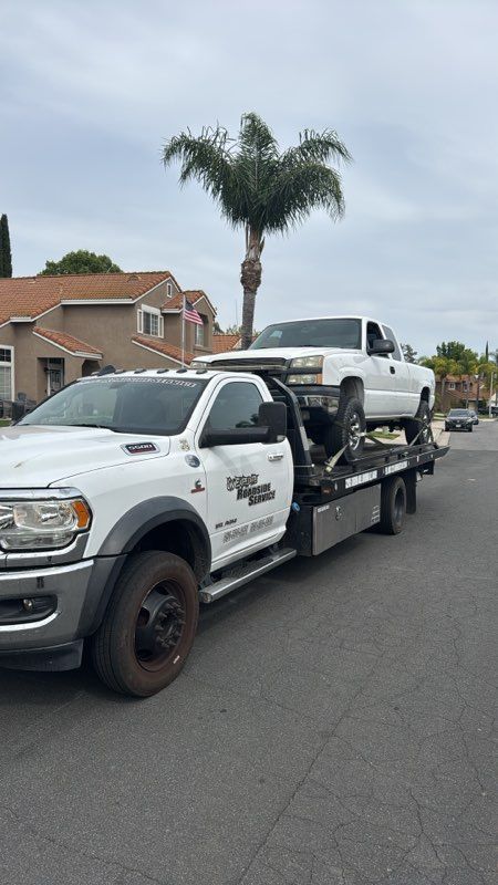White Smart car being towed on a flatbed tow truck in front of a two-story house.