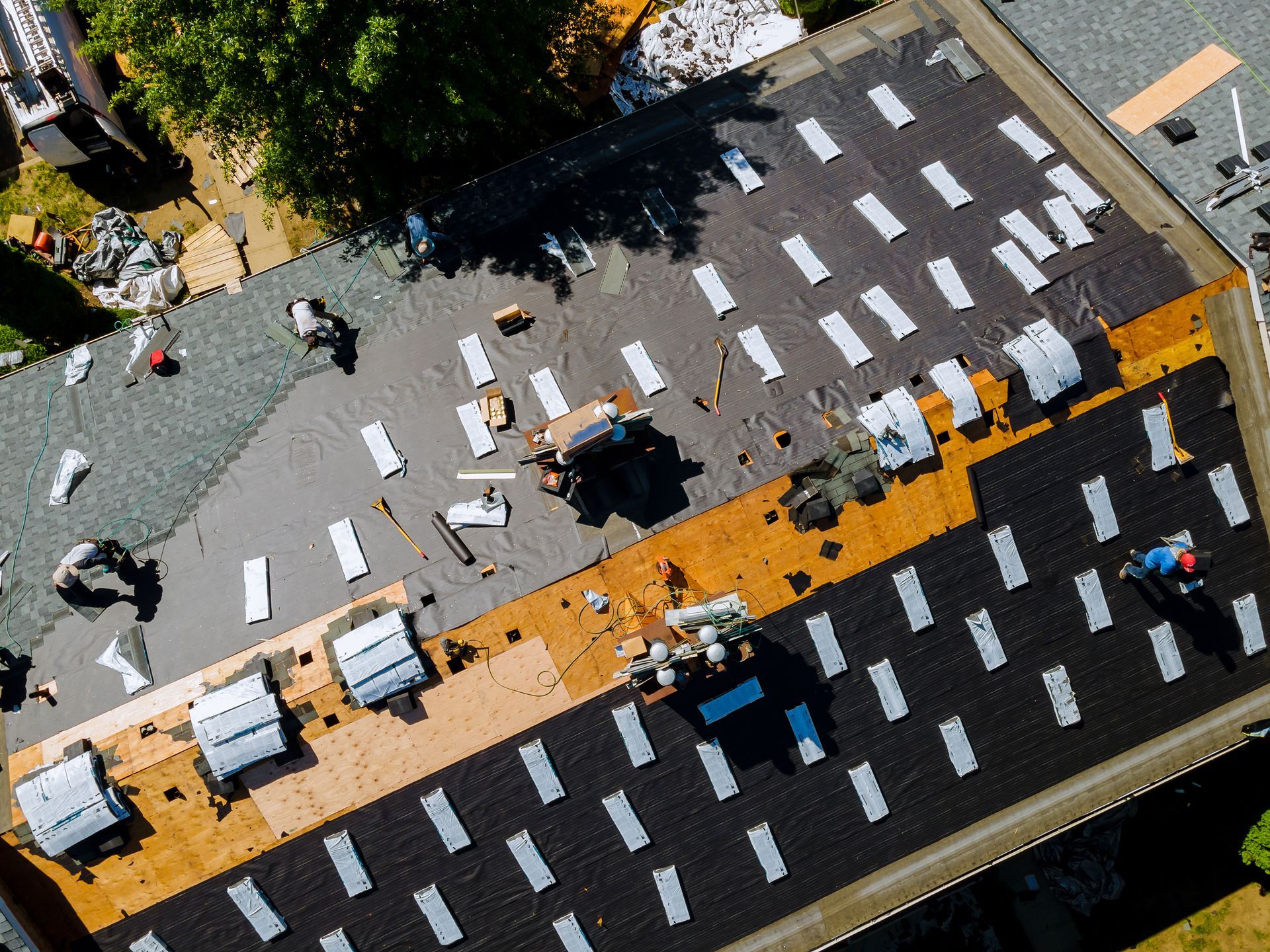 Workers installing new roofing materials on a large residential roof under sunny weather.