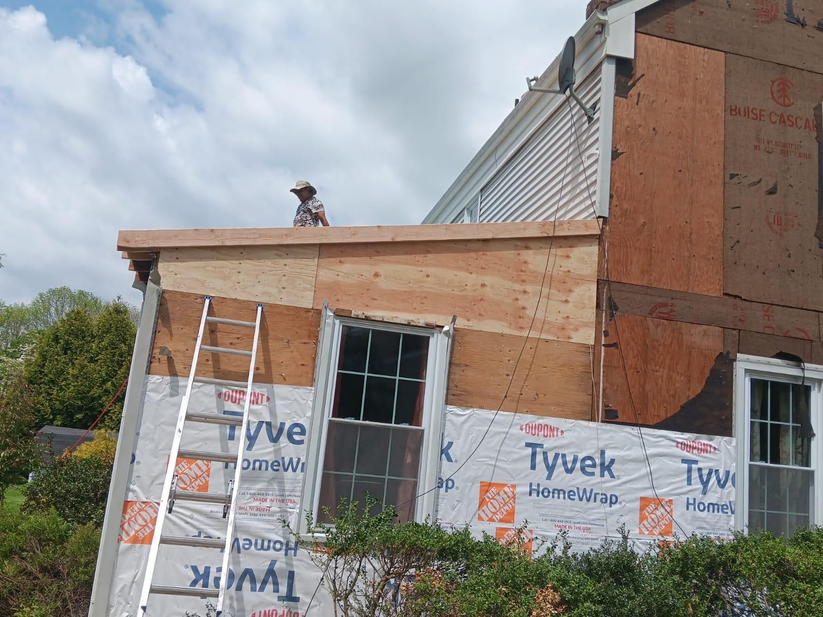 A Man Is Standing on the Roof of a House With a Ladder — Burlington, NJ — AD Roofer Siding & Gutters