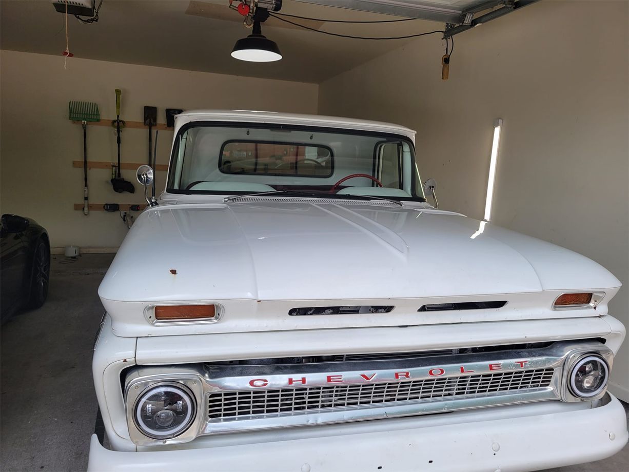 White vintage Chevrolet pickup truck parked in a garage with tools on a wall.
