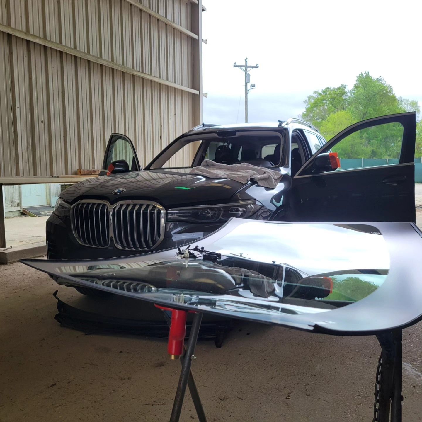 Damaged black BMW SUV with open doors and a detached hood in a repair shop.