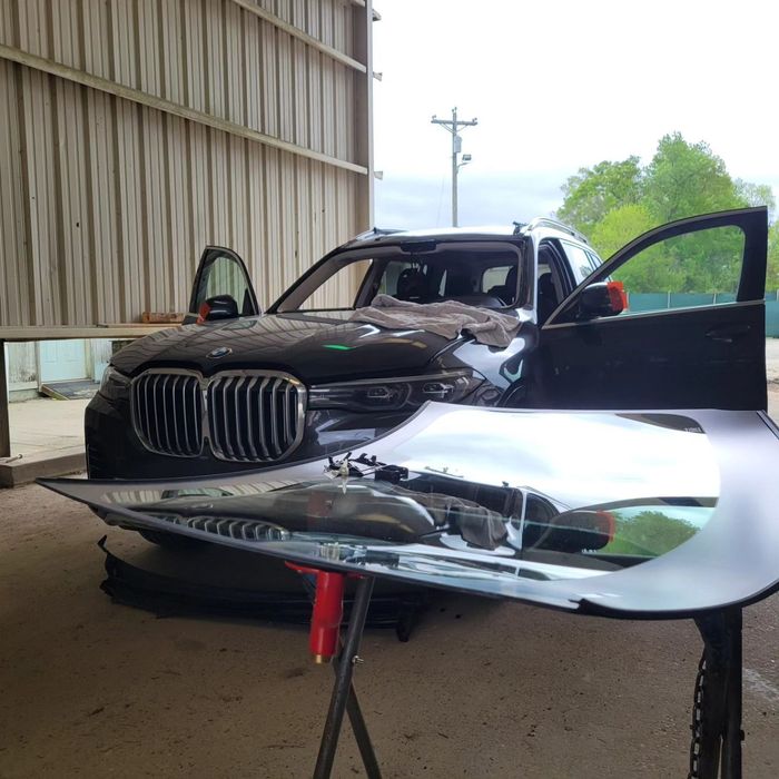Damaged black BMW SUV with open doors and a detached hood in a repair shop.