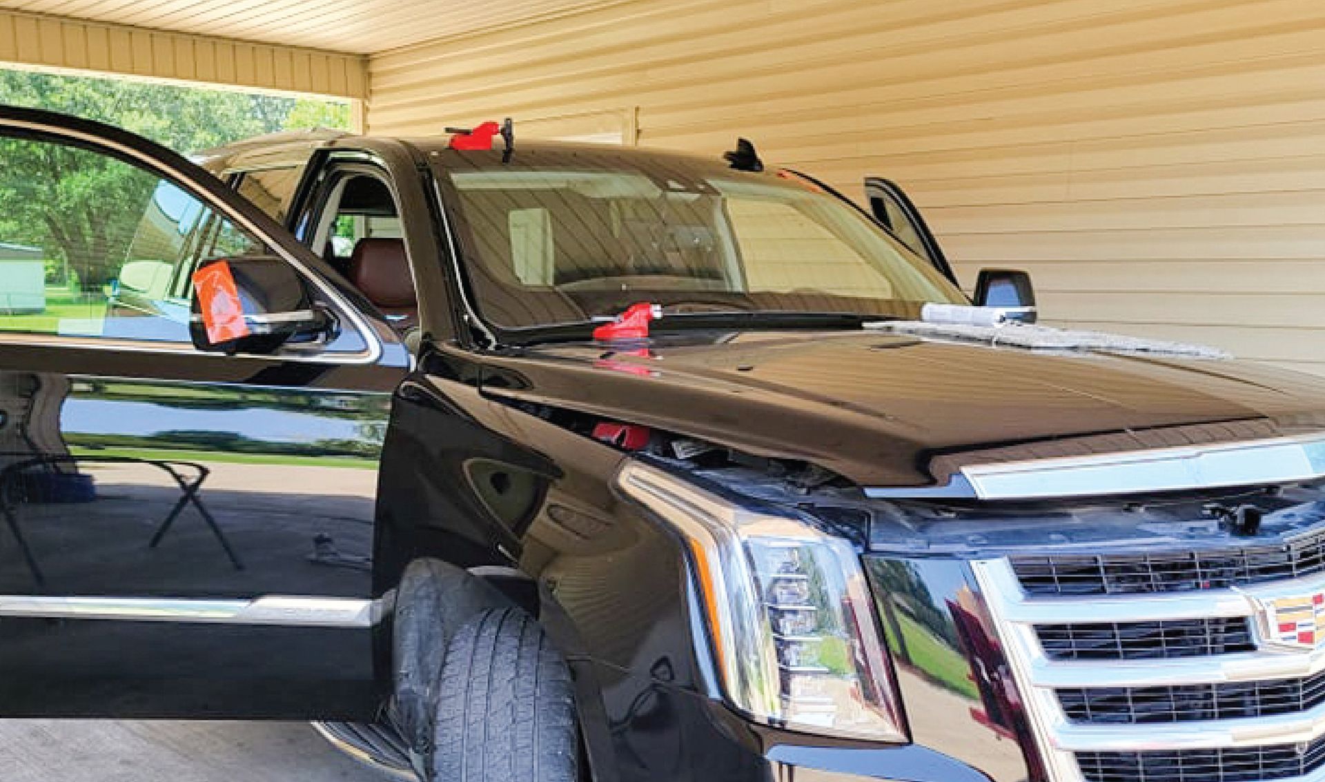 Black Cadillac SUV with open doors and hood, parked under a carport, tools on the hood.