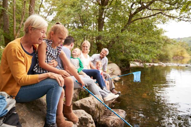 Family sitting on rocks by a river, using a net, enjoying a sunny day.