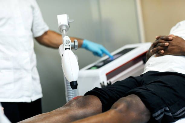Person receiving laser therapy on their knee. Healthcare professional adjusts the device.