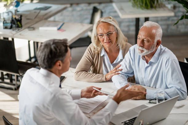 Financial advisor meeting with a senior couple at a table; documents and laptop present.