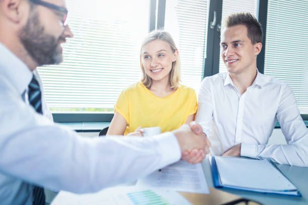 Man in suit shakes hands with a couple at a table in an office. They smile.